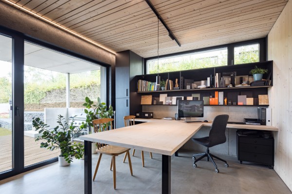 Büro mit Einbaumöbeln, Sichtbetonboden und stimmungsvollem Lichtambiente sowie einer großzügigen Glasfassade mit Blick in den Garten