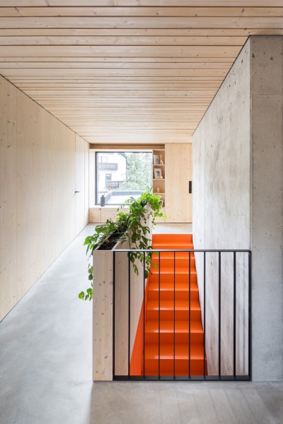 Besonderes Treppendesign. Zwischen Holz und Sichtbetonwand sorgt die orangene Treppe für die perfekte Inszenierung des Treppenhauses. Zudem wurde die Holzbrüstung mit einem eingelassenen Pflanzbeet versehen um den Treppenraum nicht nur minimalistisch, sondern auch wohnlich zu machen